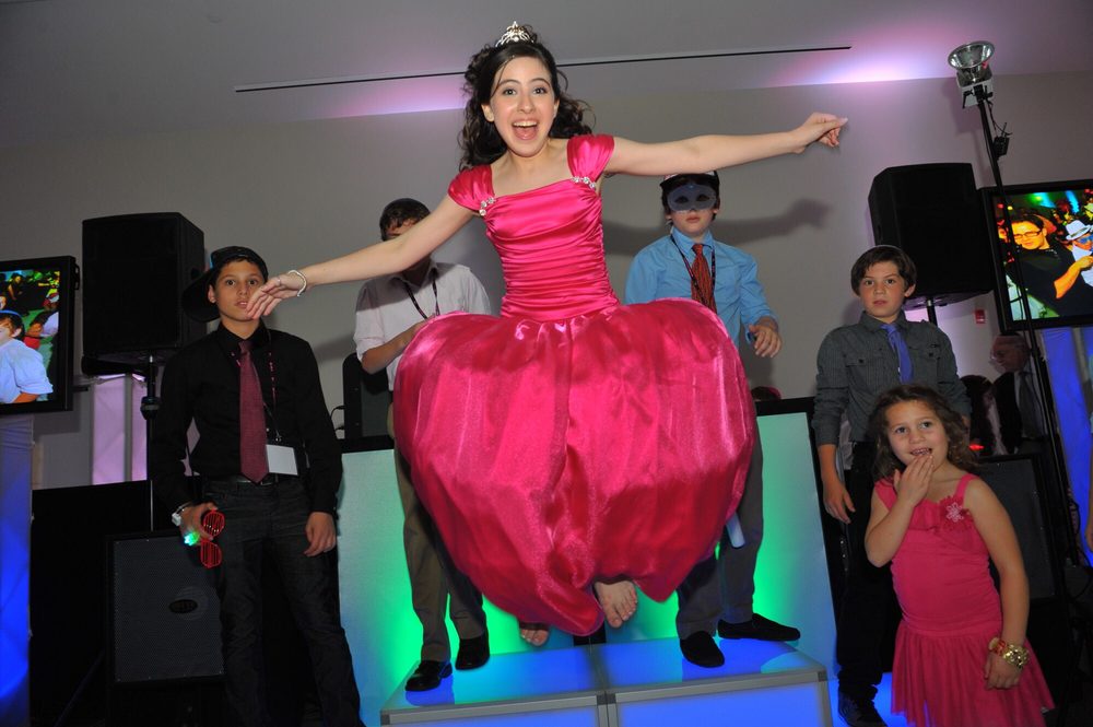 Bat Mitzvah girl in a pink gown jumping off a lit LED stage